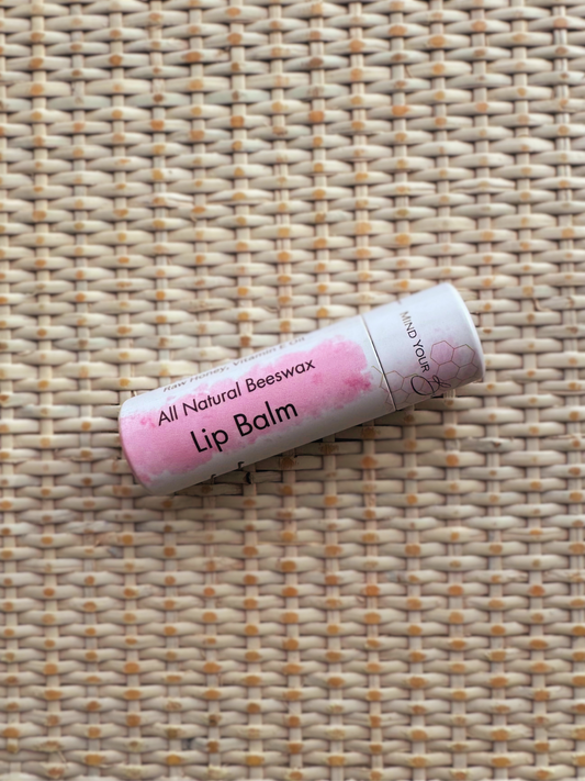 All natural beeswax lip balm, in a pink and white tube on a woven background