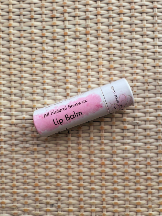 All natural beeswax lip balm, in a pink and white tube on a woven background